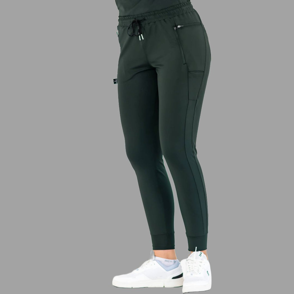 Side view of women's scrub joggers 920 super stretch bottle green with hands in pockets.