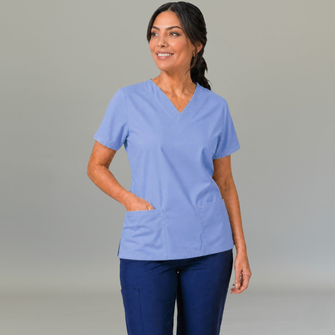 Vista frontal de filipina médica 502 azul plumbago con cuello en V, modelo con manos en los bolsillos.