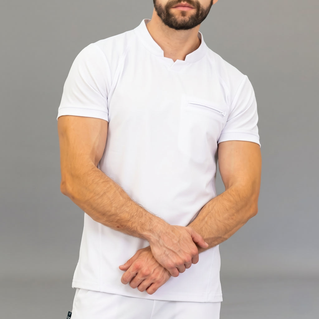 scrubs-blanco-torso-cruzado.jpg: "Hombre con brazos cruzados luciendo la filipina quirúrgica Est. 910 en color blanco, con detalle del bolsillo del pecho con cierre y cuello con abertura en V."